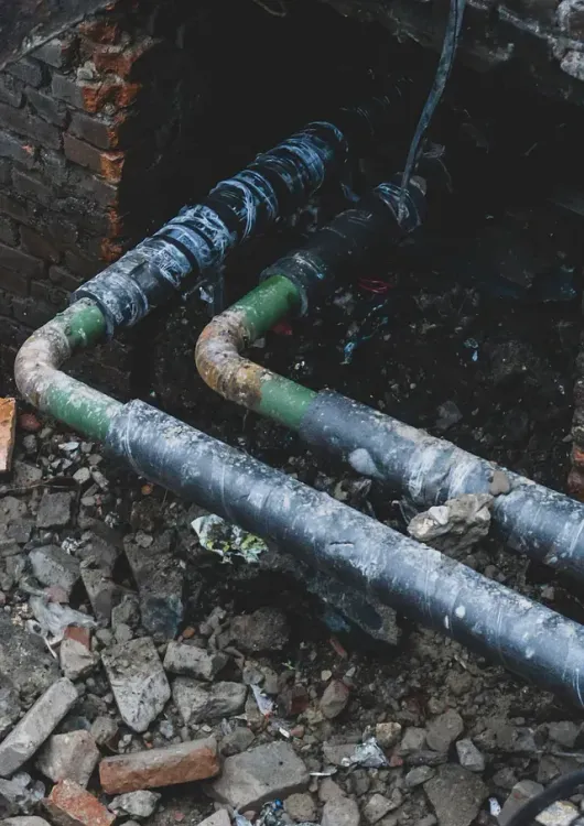 Un par de tuberías están tiradas en la tierra junto a una pared de ladrillos.