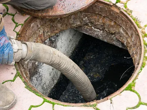 Un hombre está bombeando agua hacia una tapa de alcantarilla con una manguera.
