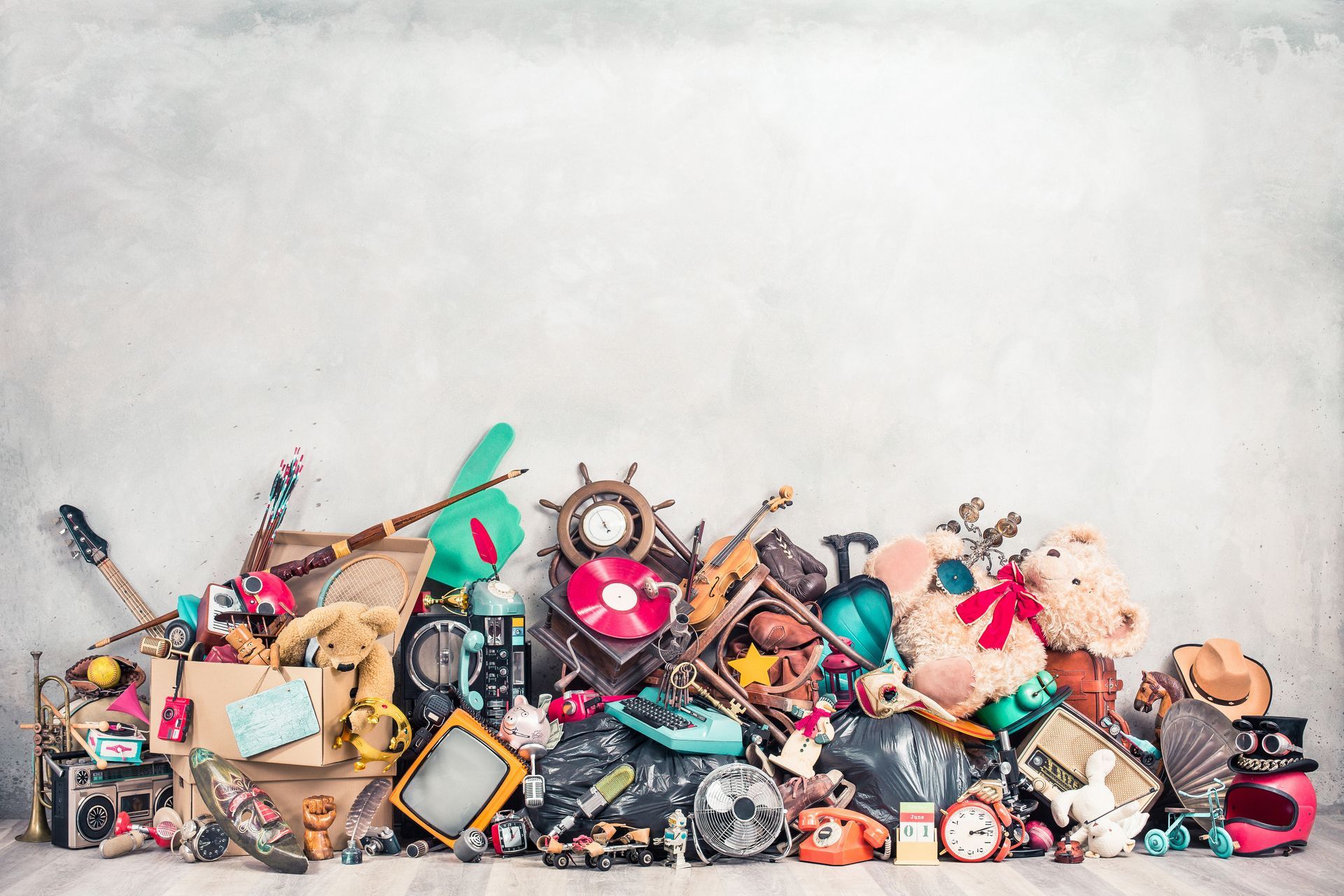 Un tas de jouets et bibelots anciens de toutes sortes, éparpillés le long d'un mur sur un sol blanc.