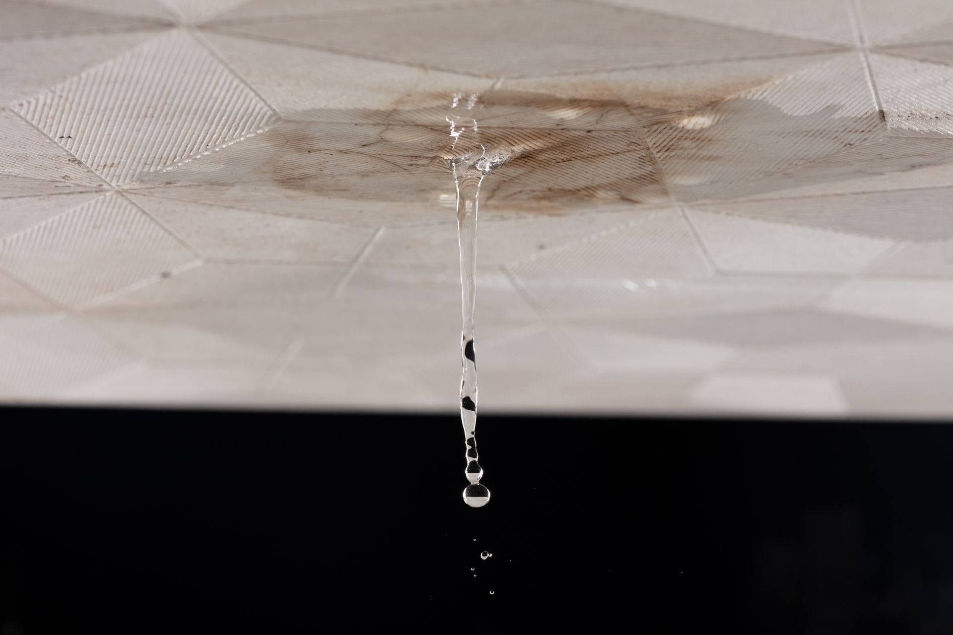 Des gouttes d'eau ruisselant d'un plafond blanc à travers une tache brune sur un fond sombre