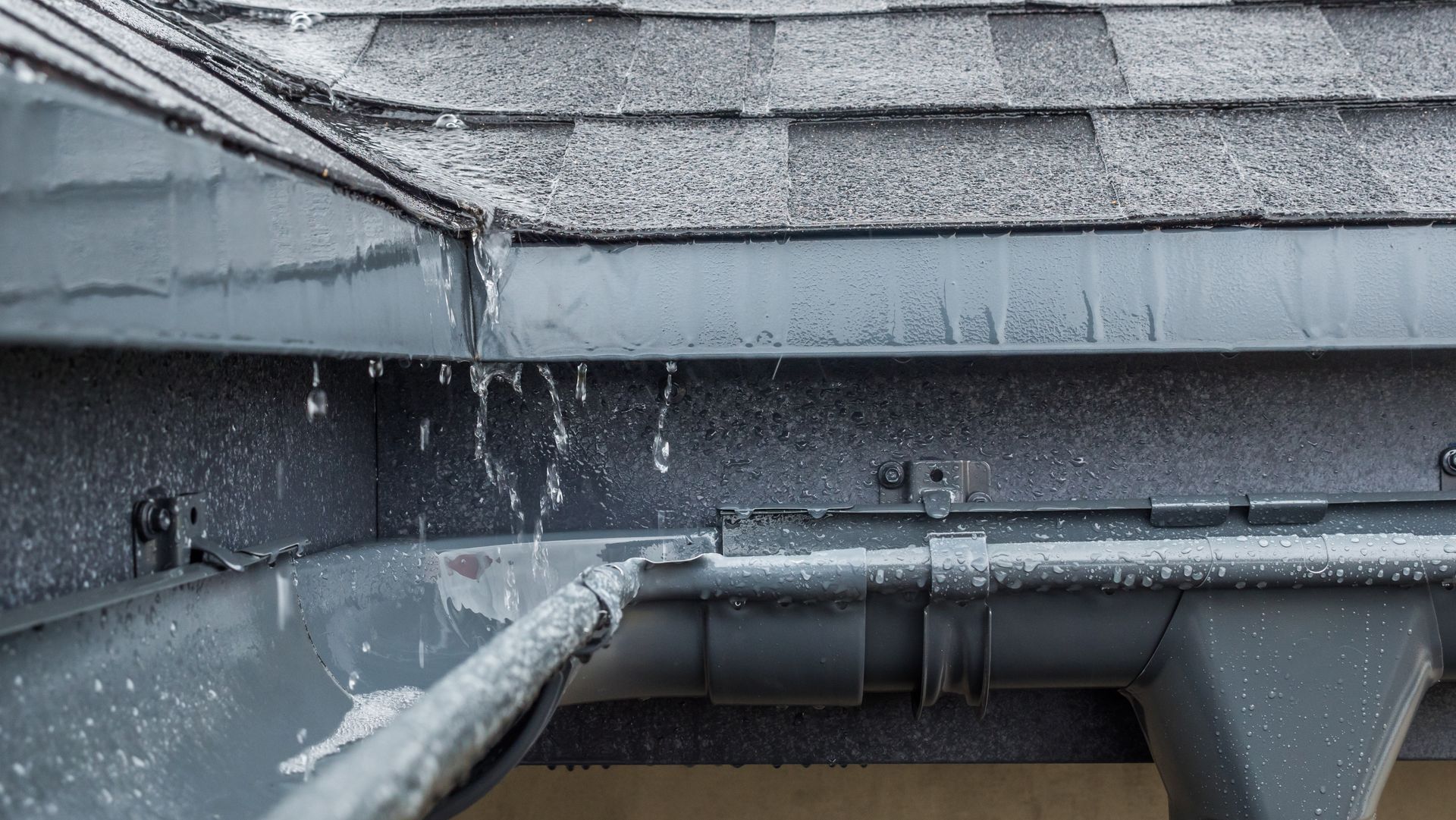 Des gouttes de pluie pendent d'un bord de toit gris au-dessus d'une gouttière en hiver