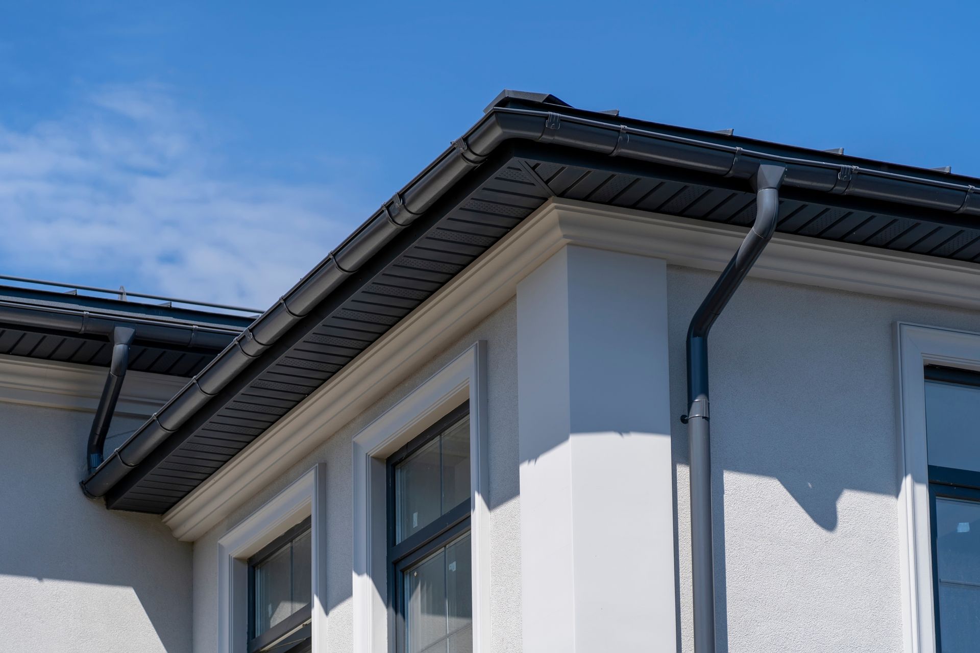 Gros plan sur la façade d'une maison blanche avec un toit gris et un ciel bleu au-dessus.