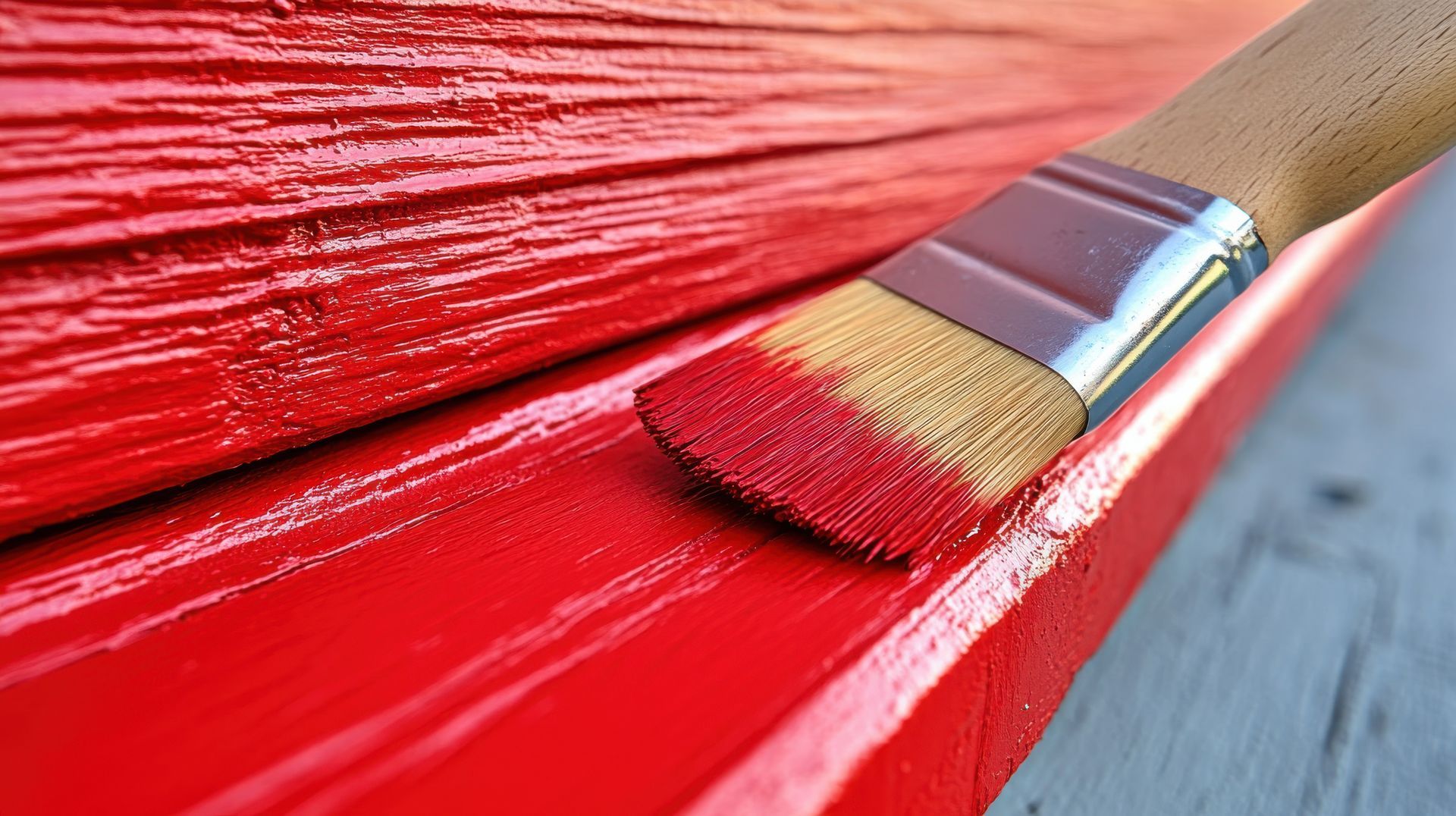 Gros plan d'un pinceau appliquant de la peinture rouge sur une surface en bois