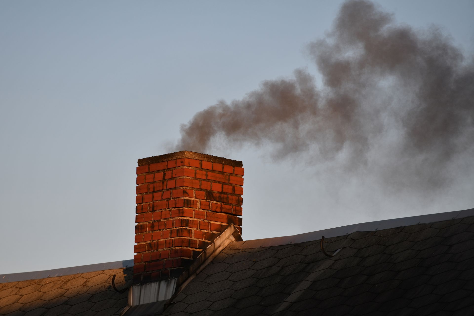 Une cheminée en briques sur un toit laisse échapper un panache de fumée noire dans le ciel