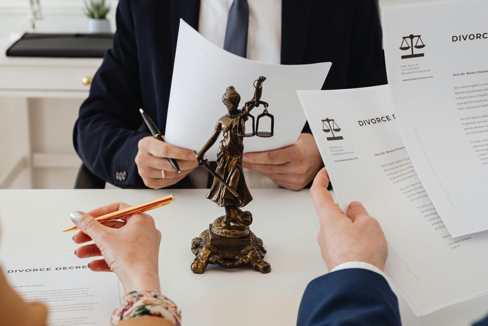 Un grupo de personas están sentadas en una mesa con papeles y una estatua de la justicia.