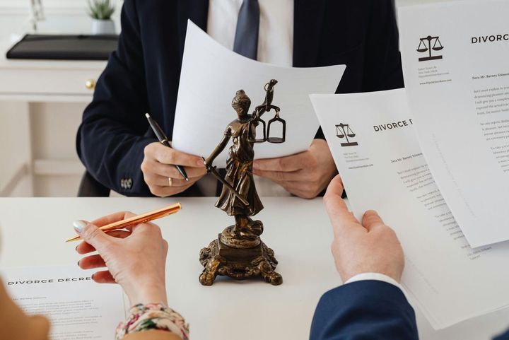 Un hombre y una mujer están sentados en una mesa con papeles y una estatua de la justicia.