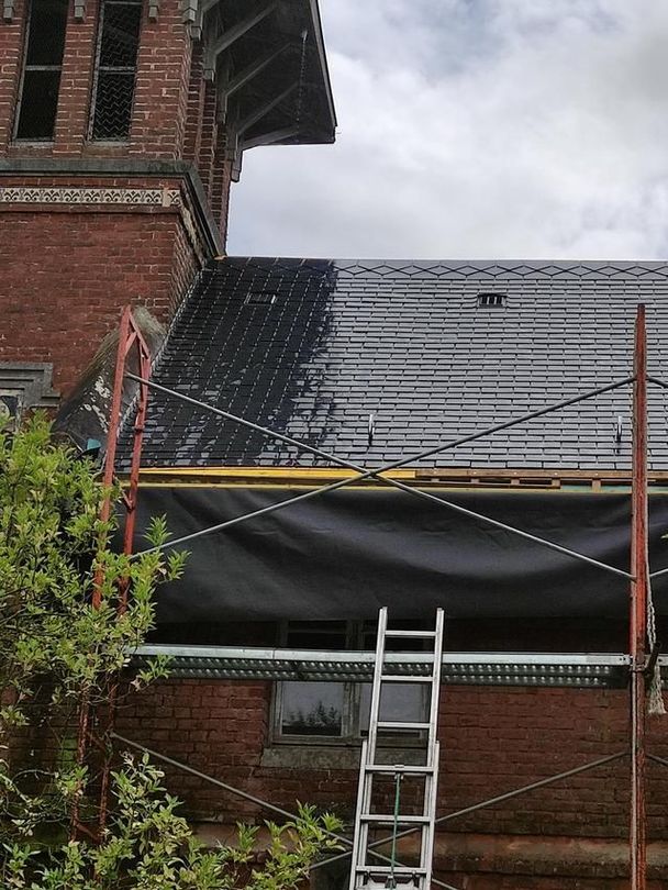 Toiture en briques d'une maison en cours de réparation : bâche noire, échafaudages et échelle appuyés contre le mur.