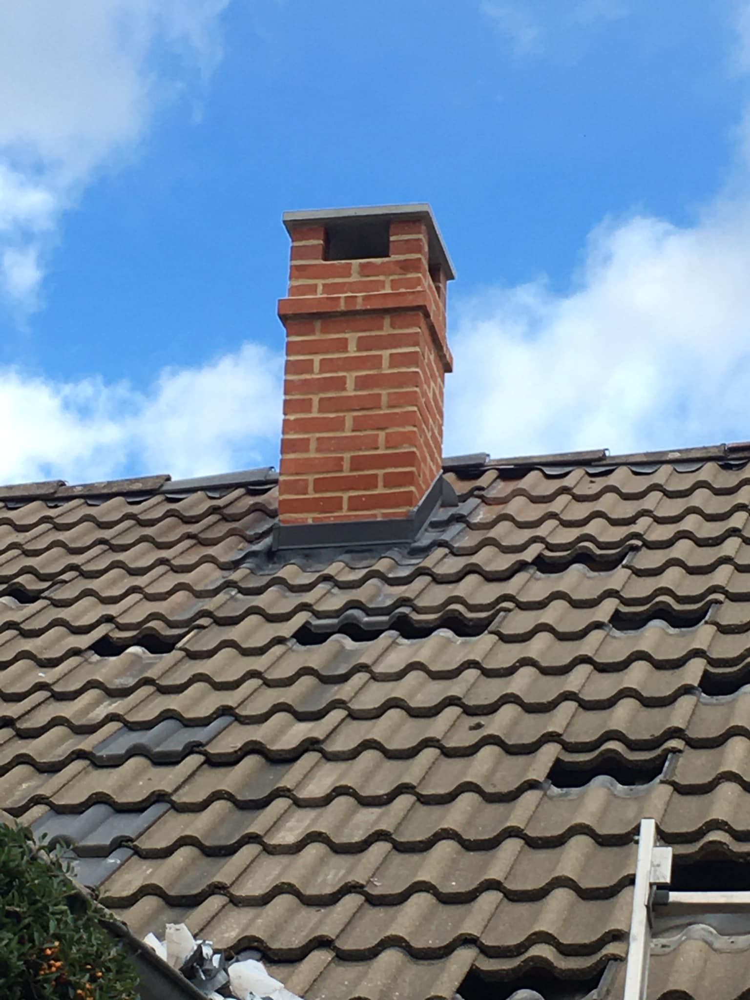 Cheminée en briques rouges sur un toit de tuiles brunes.