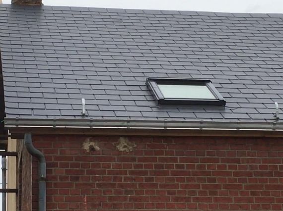 Maison en briques avec un toit en bardeaux gris et une petite lucarne au-dessus d'un mur en briques rouges.