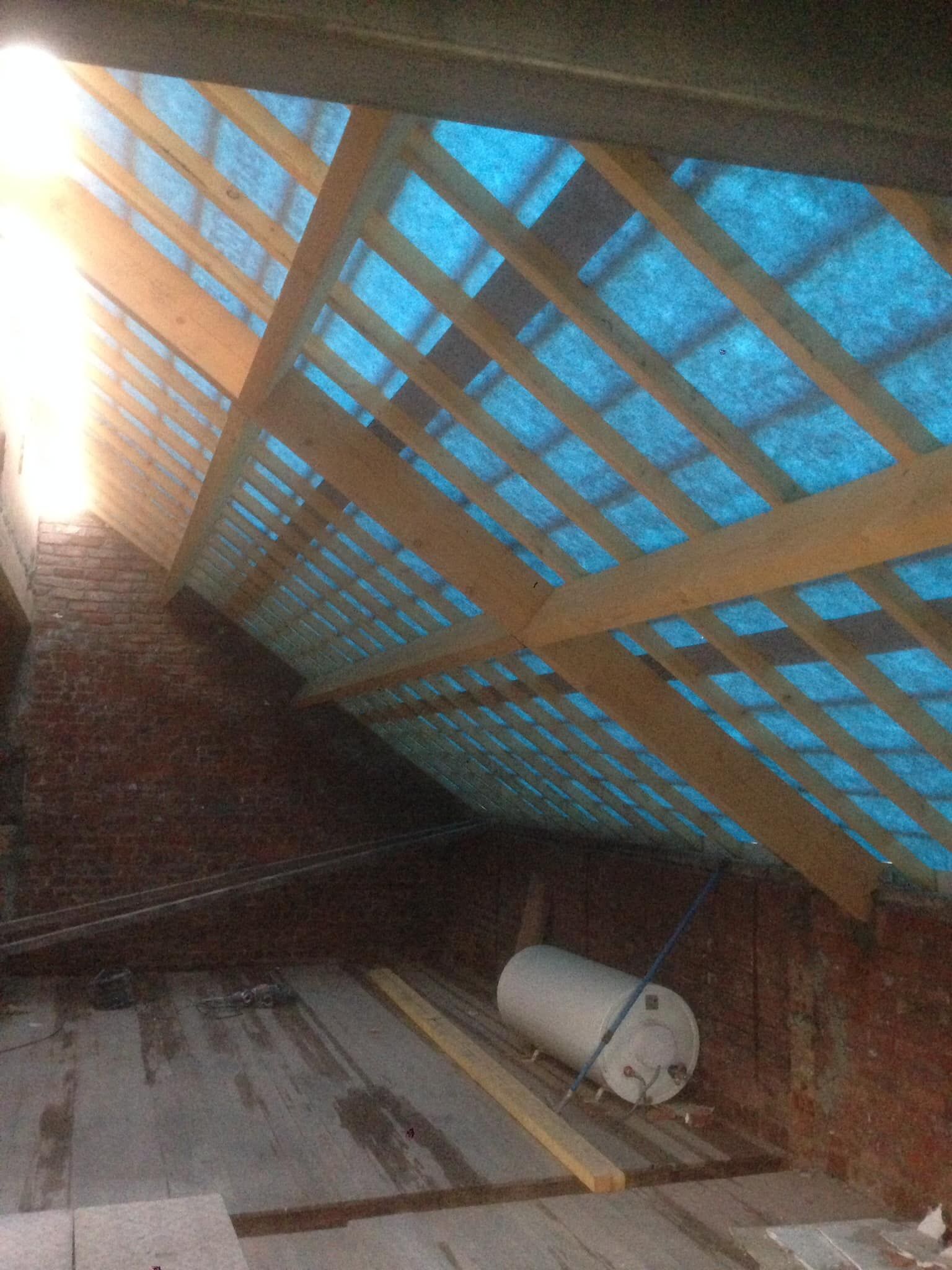 Plafond en bois d'une grange avec puits de lumière, ciel bleu visible et bonbonne de propane blanche au sol.