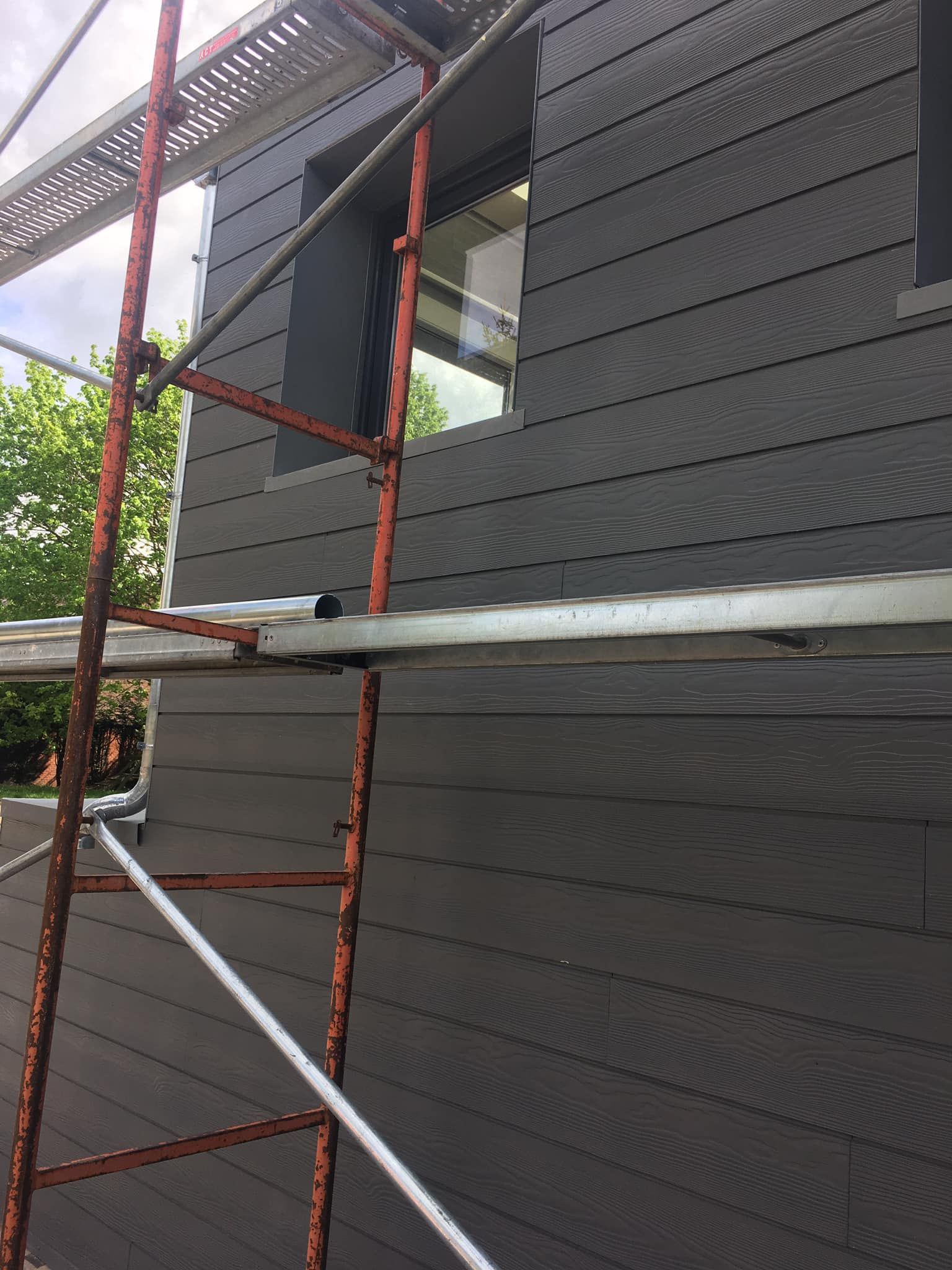 Échafaudage adossé au mur gris foncé d'une maison avec une fenêtre et un avant-toit.