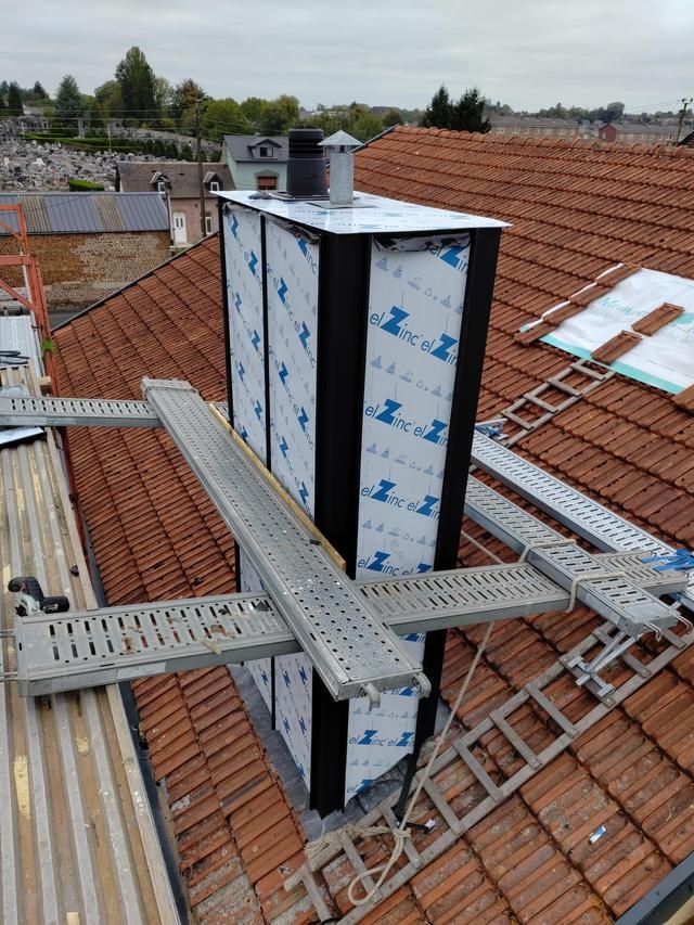Conduit de cheminée en construction sur le toit, avec échafaudages métalliques et tuiles rouges.