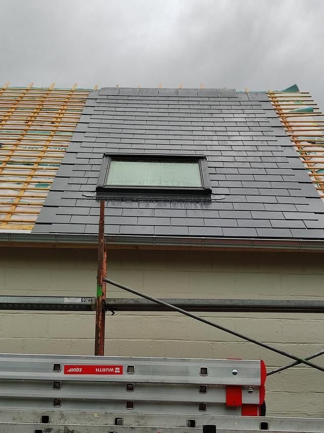 Toiture en construction avec bardeaux gris, une lucarne et un échafaudage en dessous.
