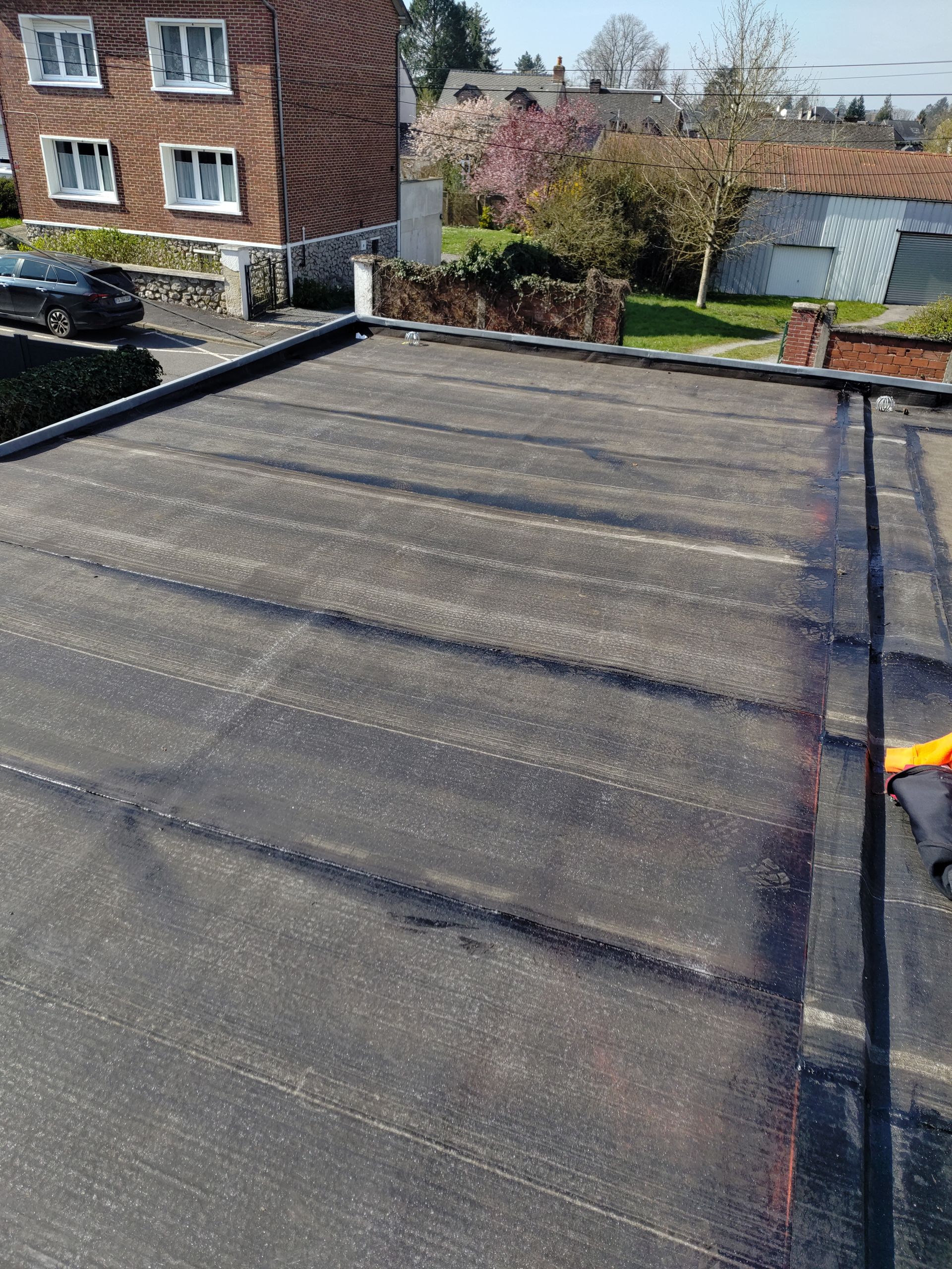 Toit-terrasse plat recouvert de gravier foncé, donnant sur des maisons en briques et un petit jardin.