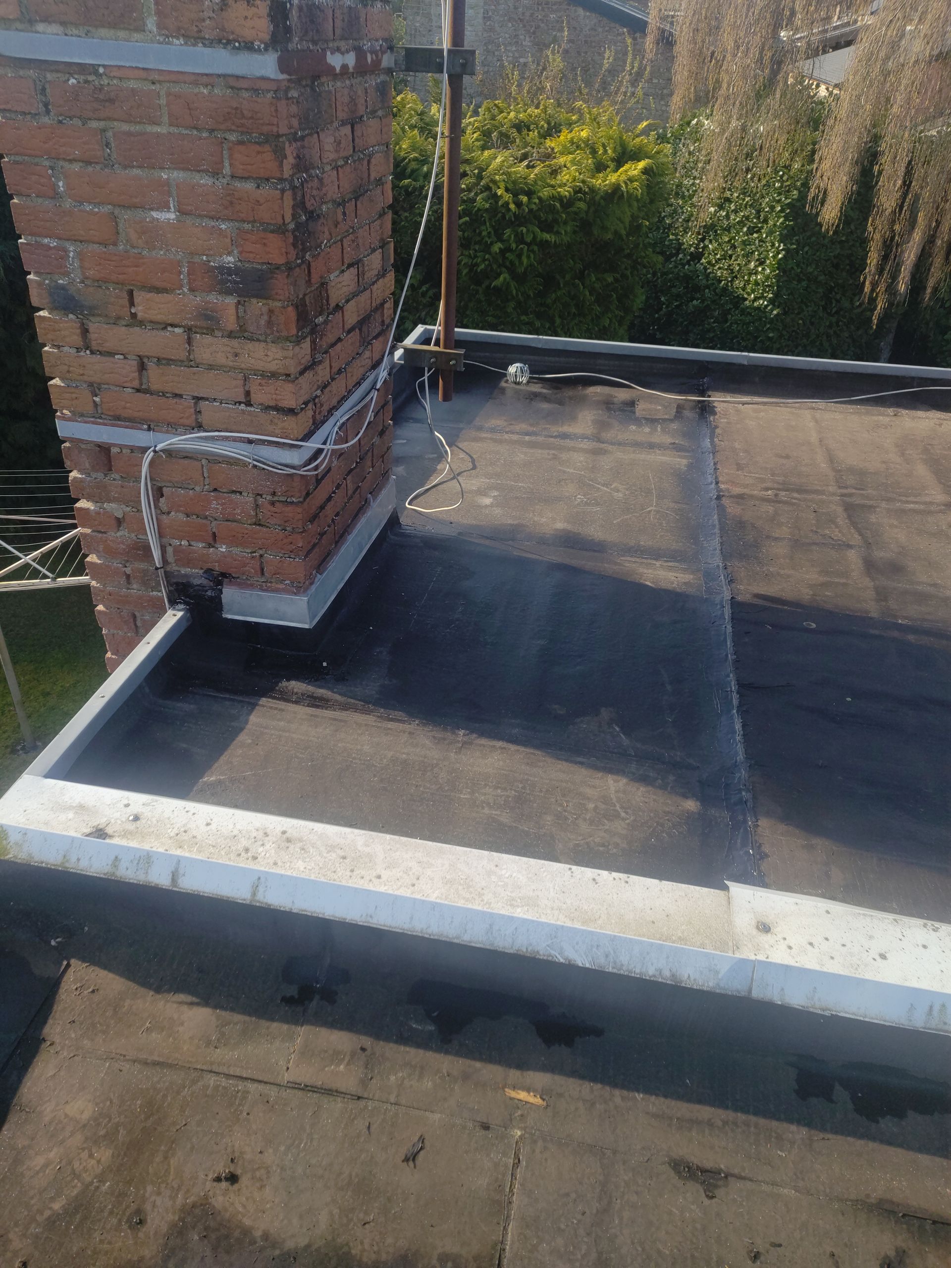 Toit plat avec cheminée en briques et toiture sombre, près d'une clôture de jardin.