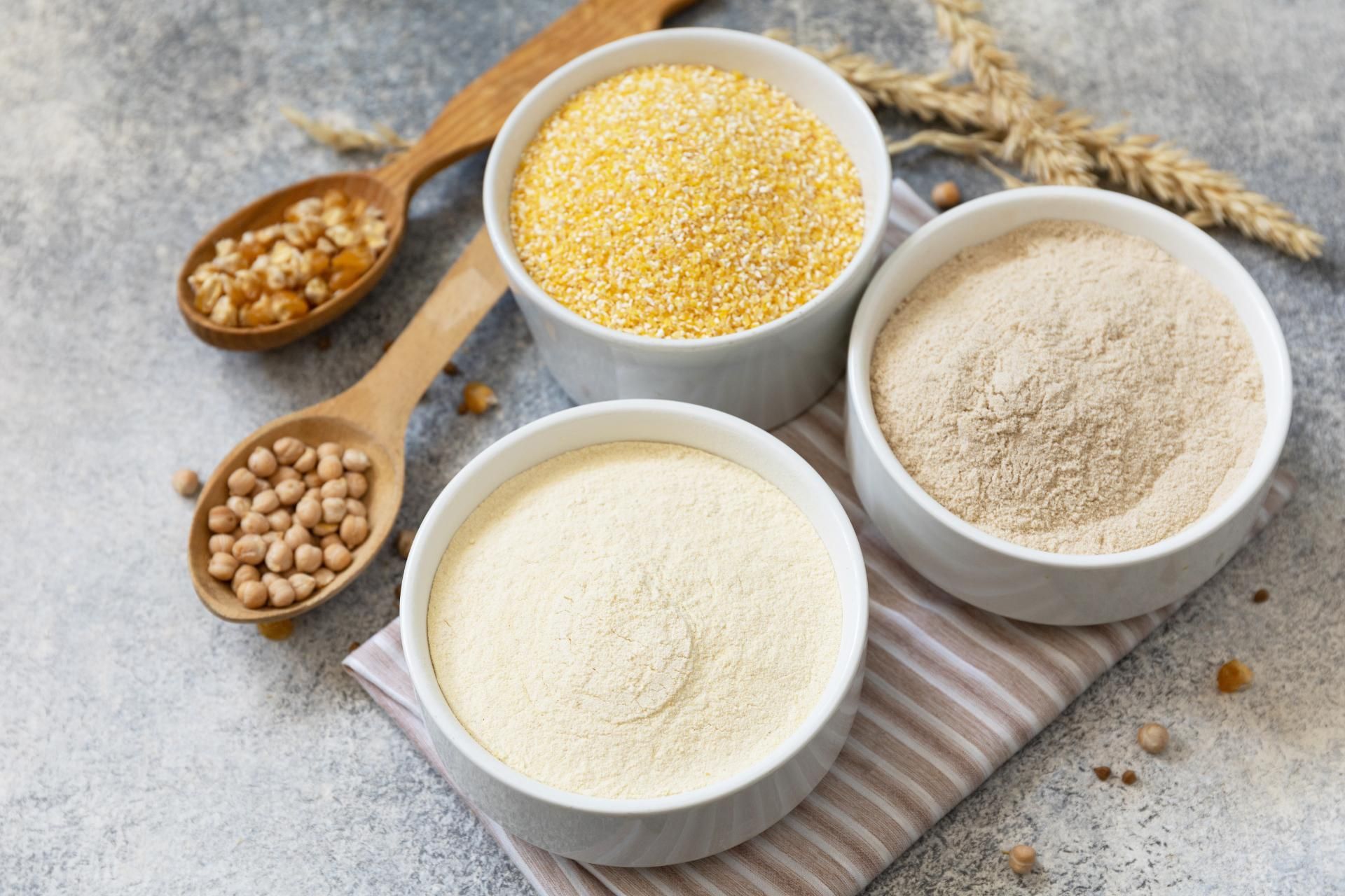 Drei Schüsseln mit verschiedenen Mehlsorten und Löffel auf einem Tisch.