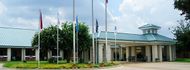 Building with teal roof and columns; flags on poles in front; cloudy sky.