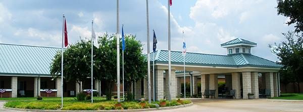 Building with teal roof and columns; flags on poles in front; cloudy sky.