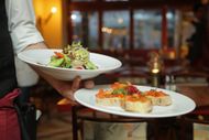 A waiter is carrying two plates of food in a restaurant.