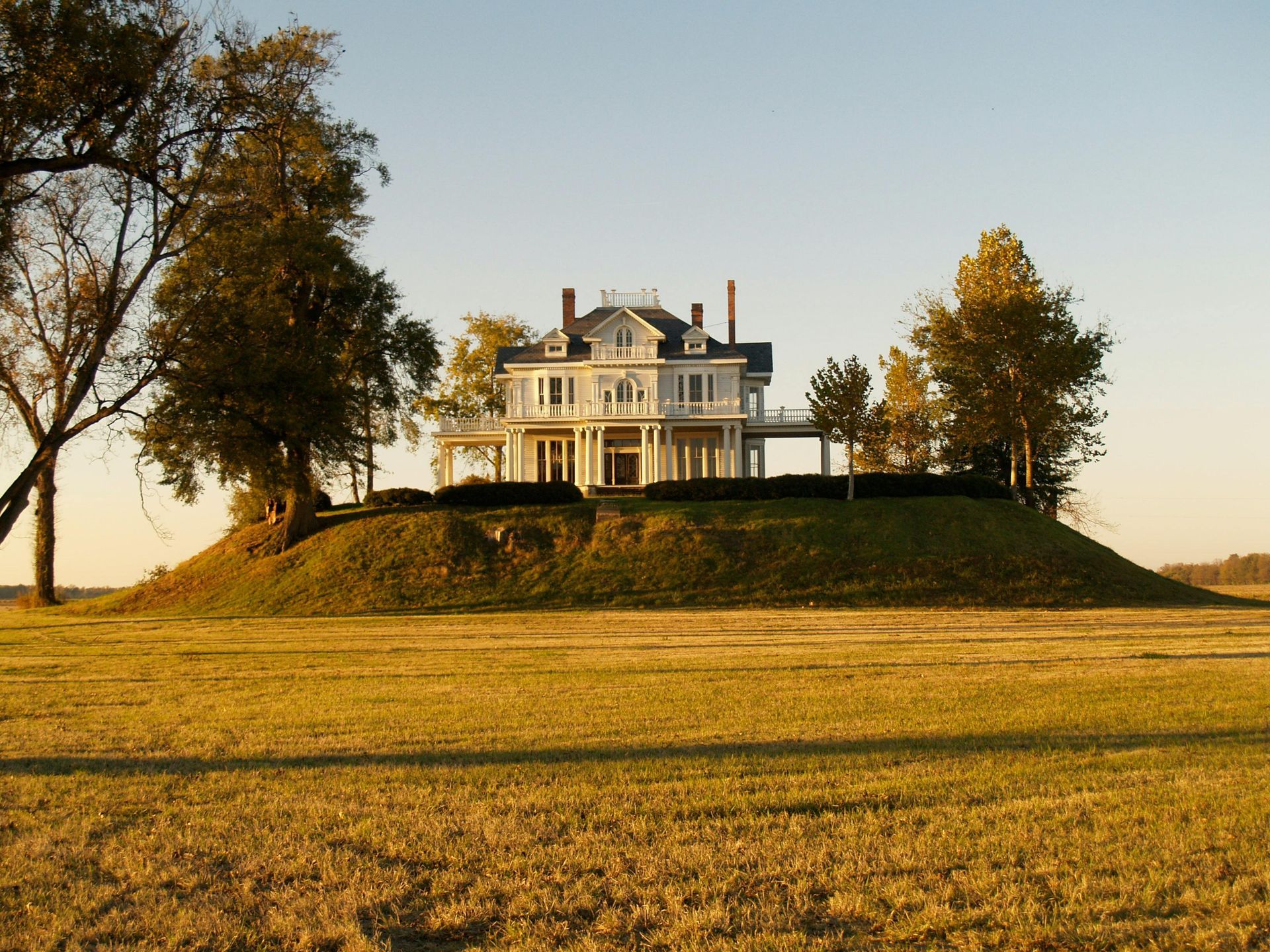A large house sits on top of a hill in the middle of a field