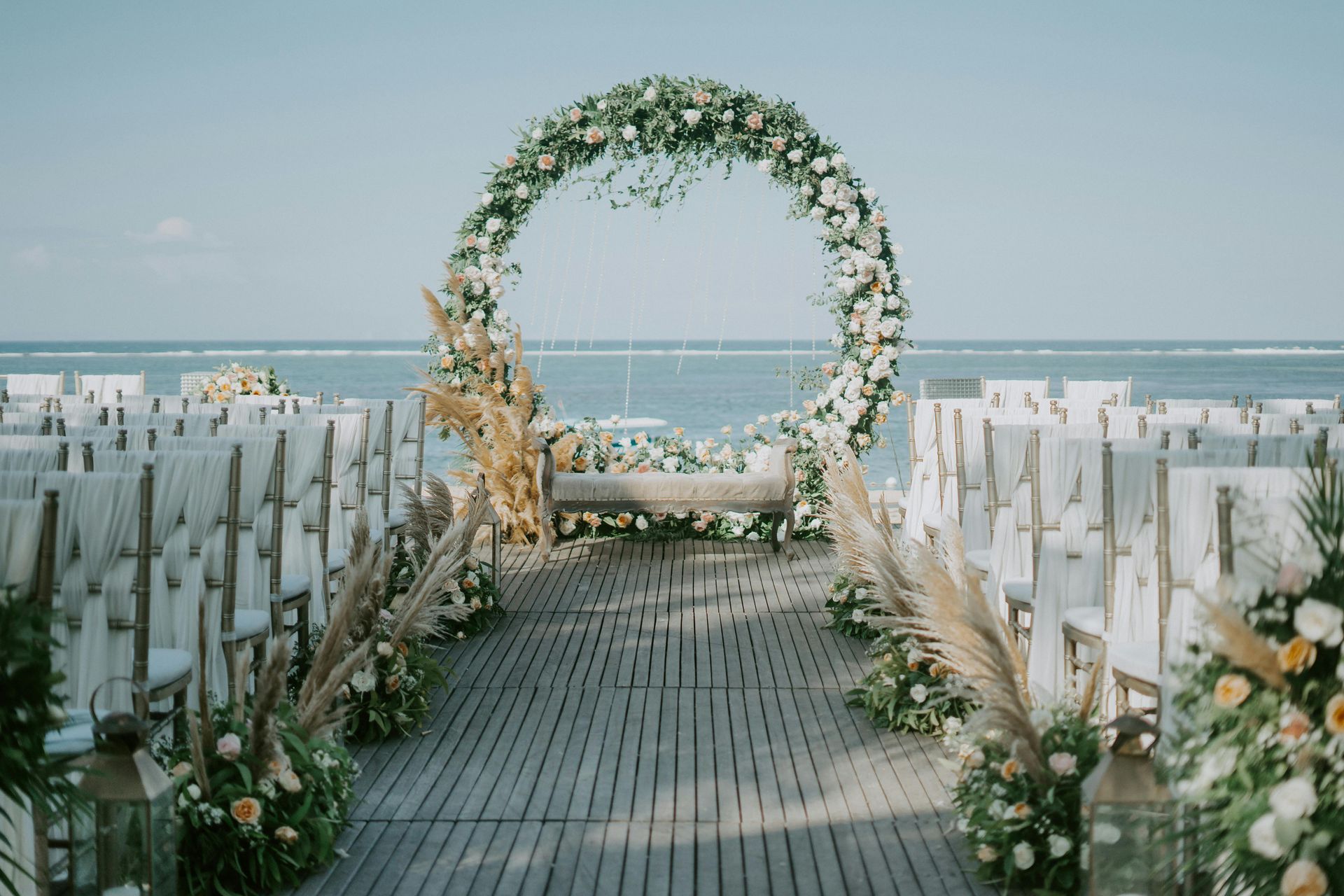 A wedding ceremony on the beach with a floral arch and chairs.