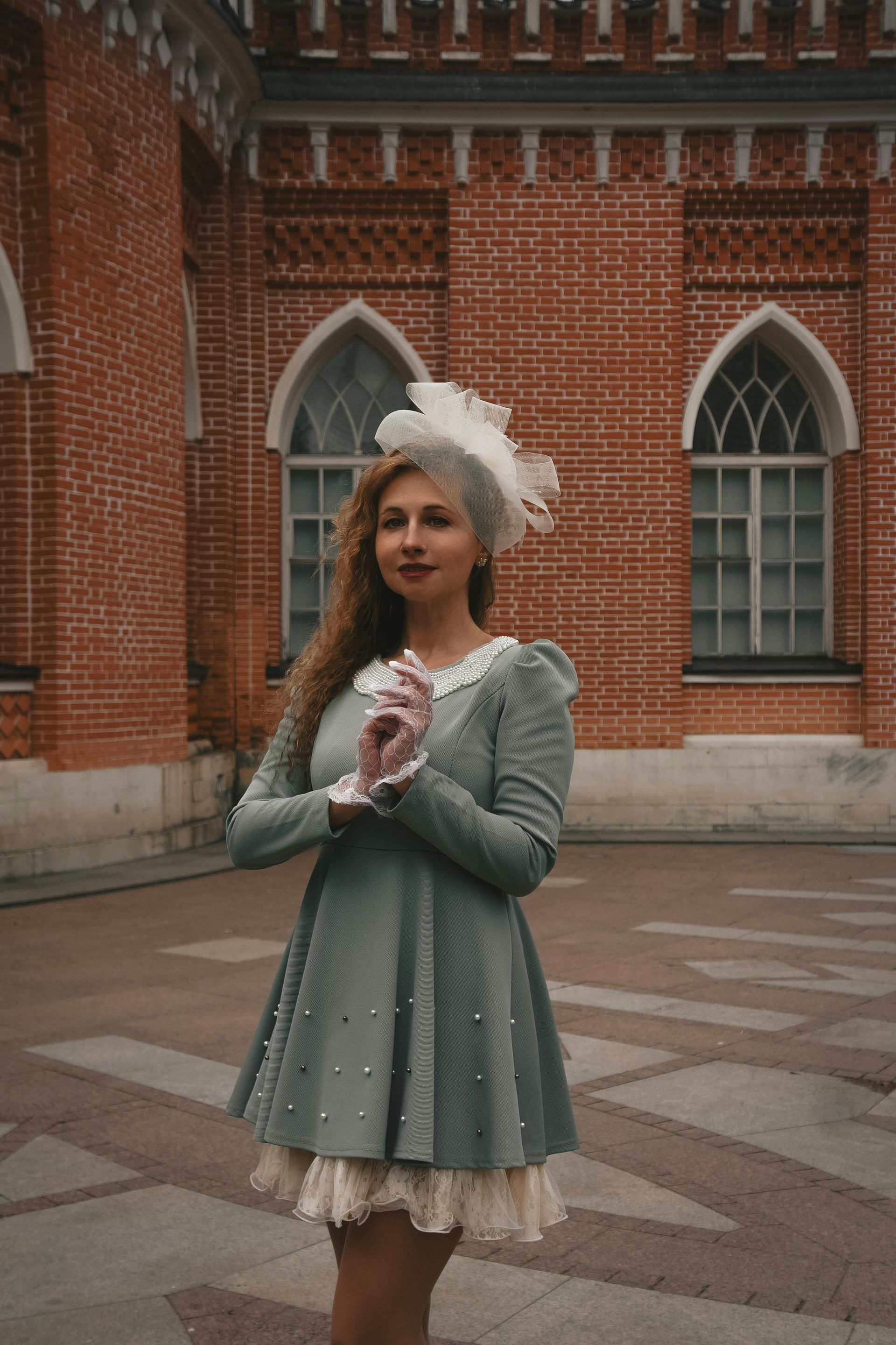 A woman in a dress and hat is standing in front of a brick building.