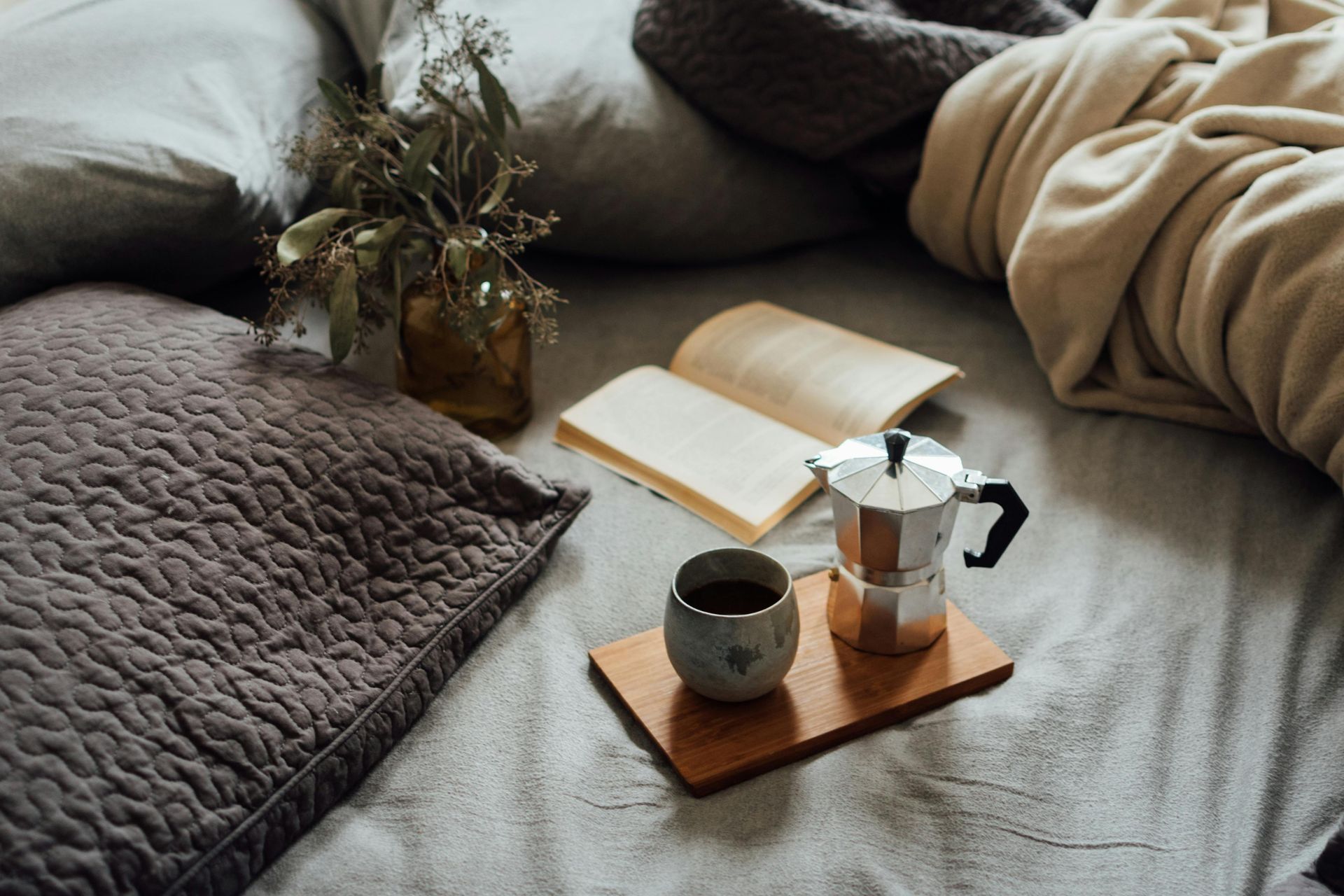 There is a cup of coffee and a book on the bed.