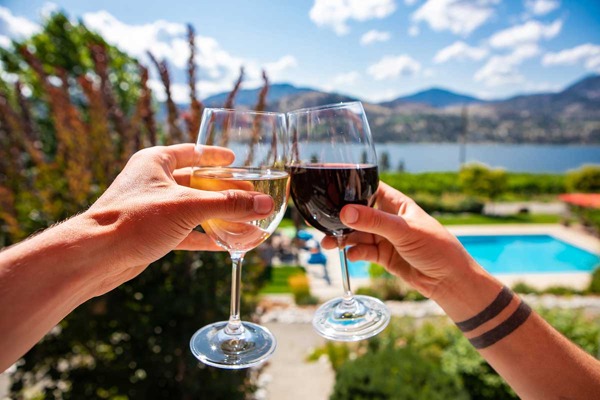 Two people are toasting with wine glasses in front of a swimming pool.