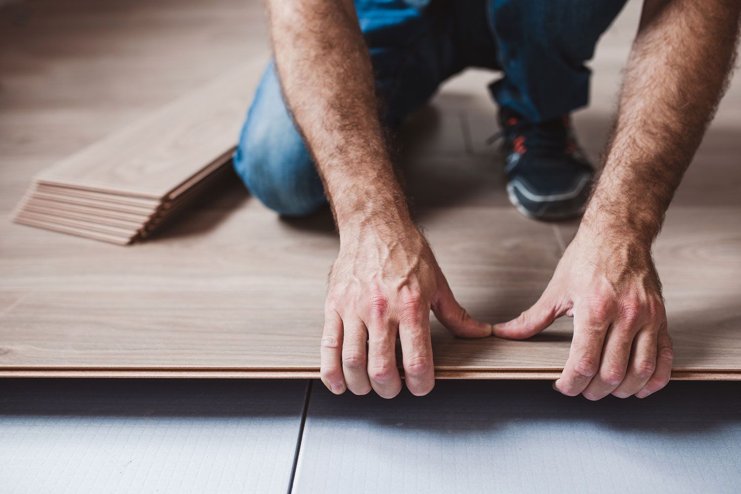 Gros plan sur un ouvrier qui pose du parquet flottant