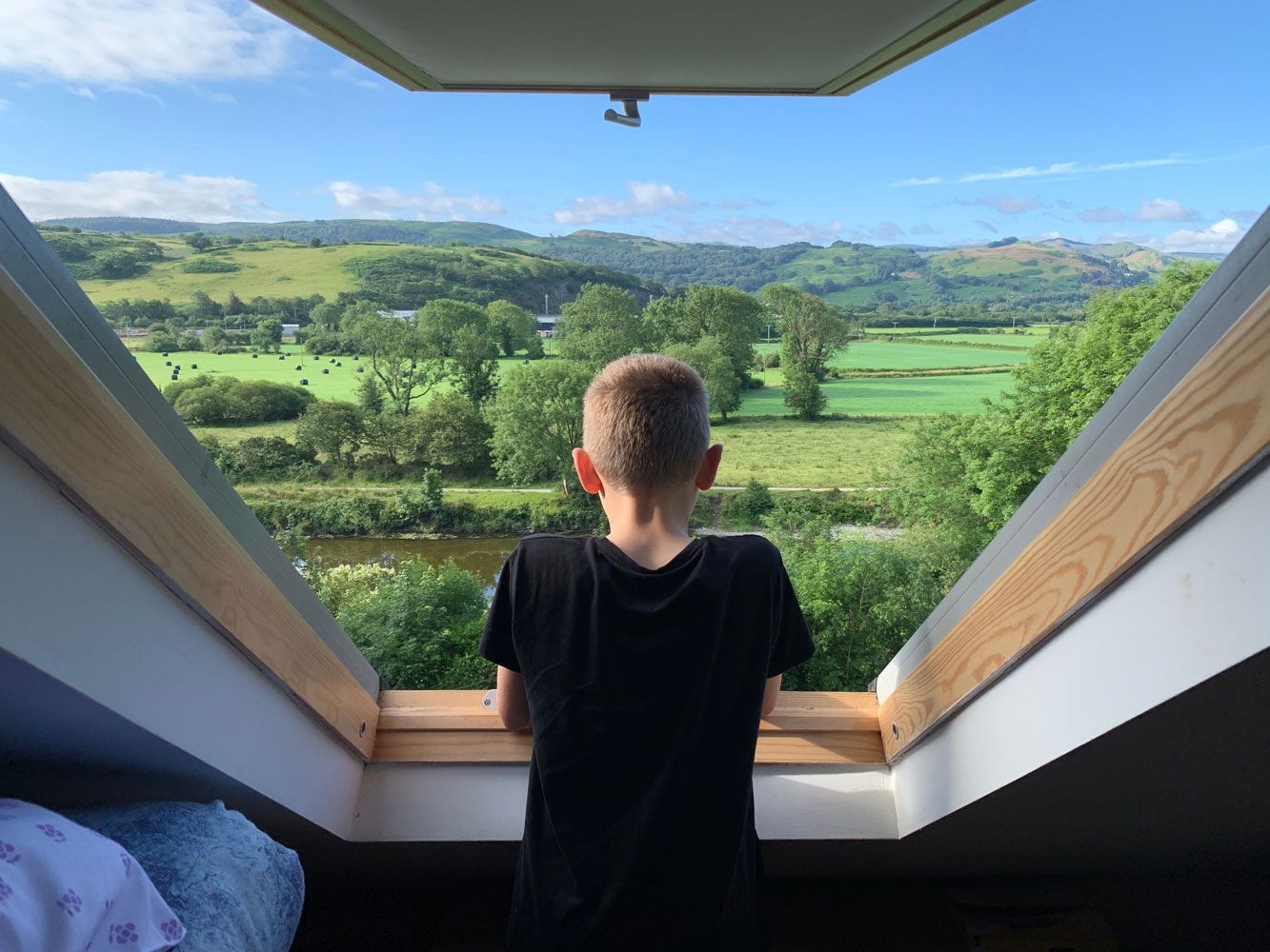 Un jeune garçon regarde par un Velux la nature au loin