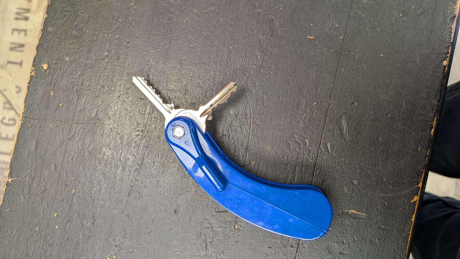 Porte-clés bleu avec deux clés sur une surface texturée foncée.