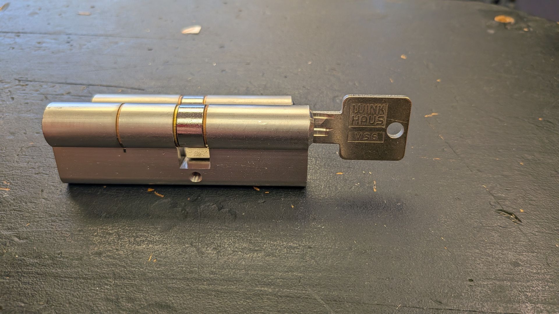 Cylindre de serrure de porte argenté avec une clé insérée, posé sur une surface sombre.