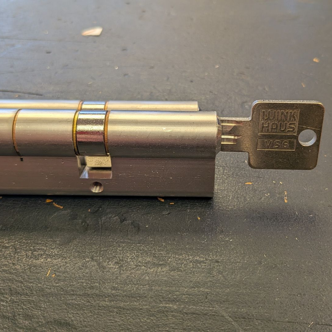 Serrure de porte argentée avec clé insérée, posée sur une surface sombre.