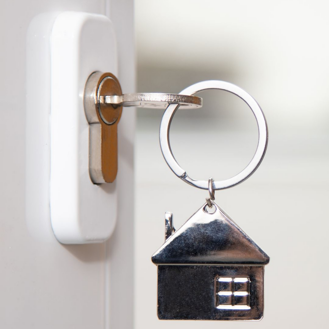 Clé insérée dans une serrure avec un porte-clés en forme de maison.