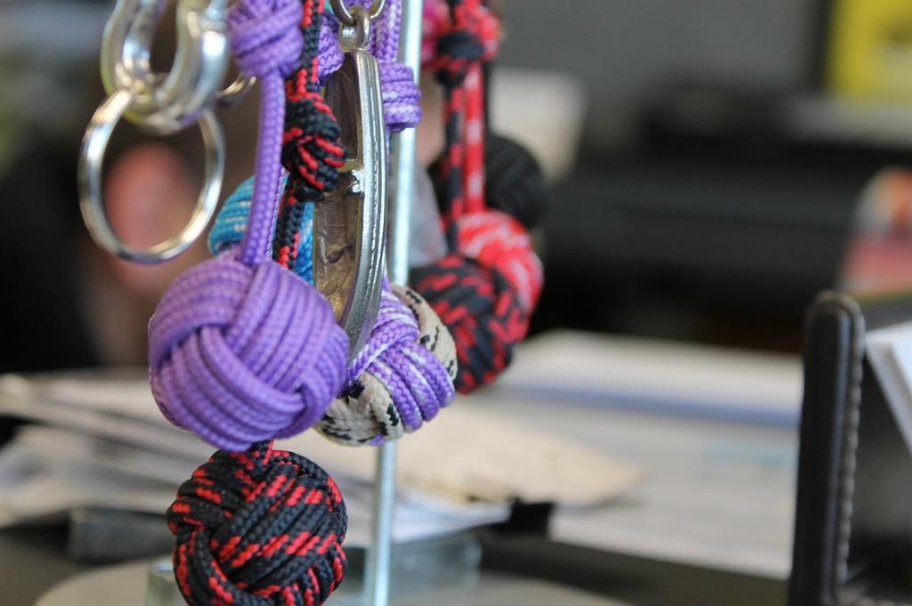 Gros plan sur des nœuds de corde décoratifs colorés suspendus à une tige métallique, sur fond flou.