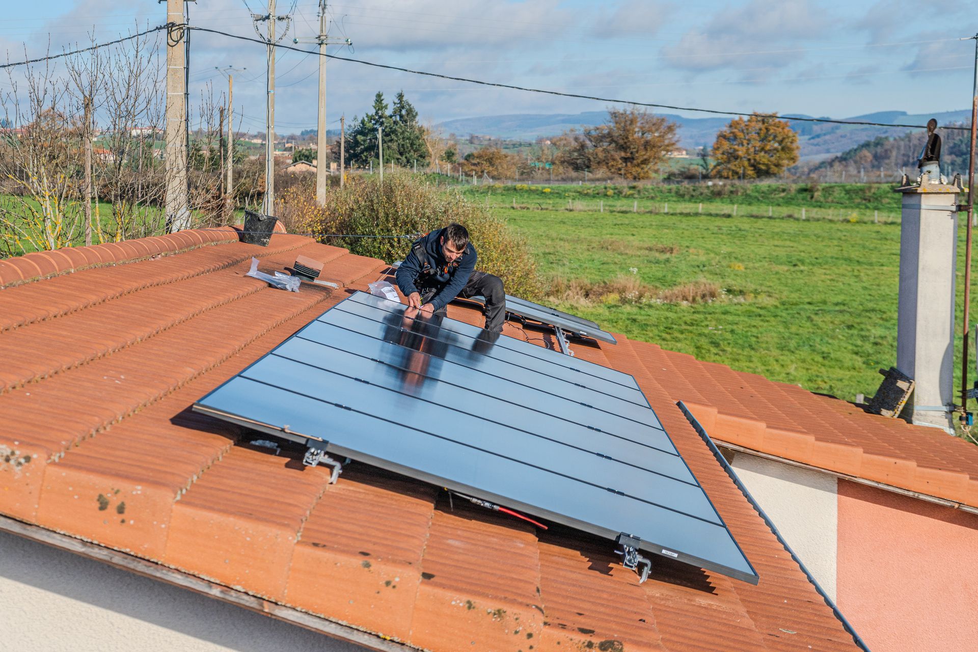 Des panneaux solaires installés sur un toit de tuiles rouges, se détachant sur un champ vert et un ciel bleu.