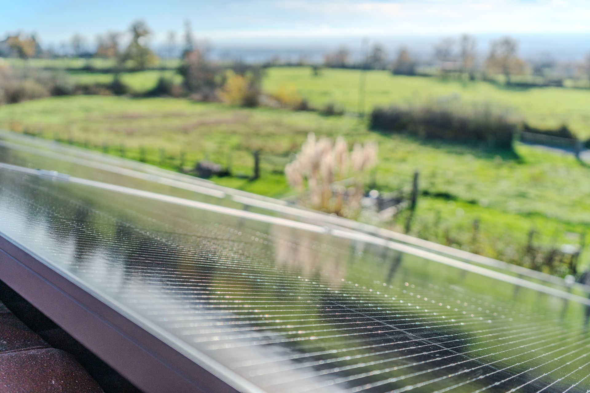 Un homme sur un toit de tuiles rouges à côté de panneaux solaires, dans un cadre rural avec un champ vert et une cheminée.