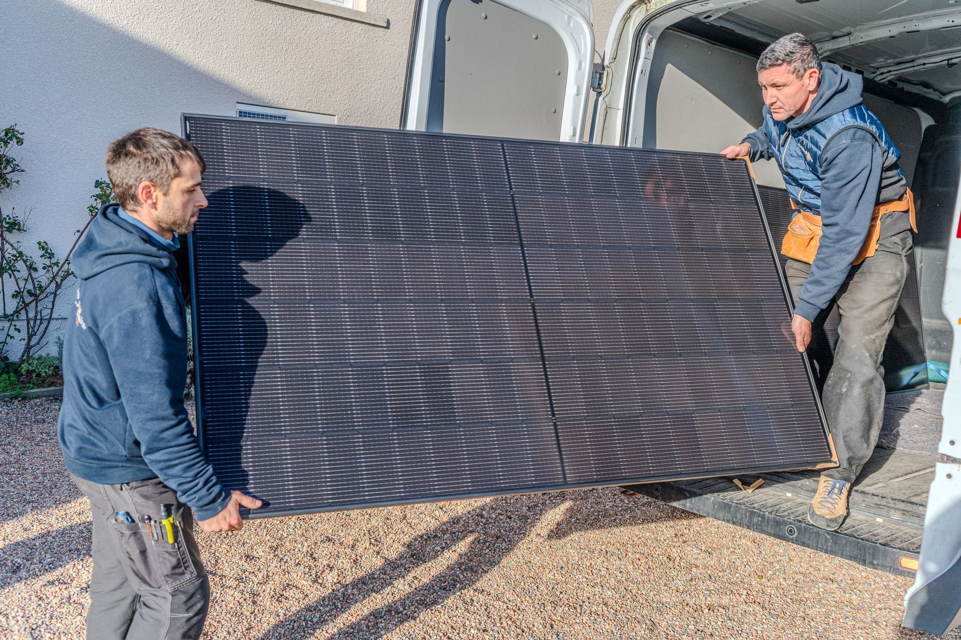 Deux ouvriers déchargent un grand panneau noir d'une camionnette.