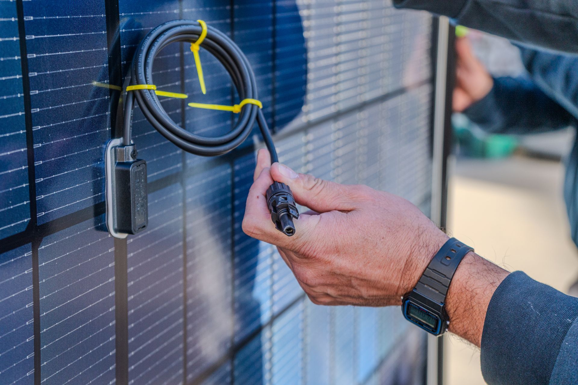 Une personne raccorde un câble de panneau solaire, portant une montre au poignet.