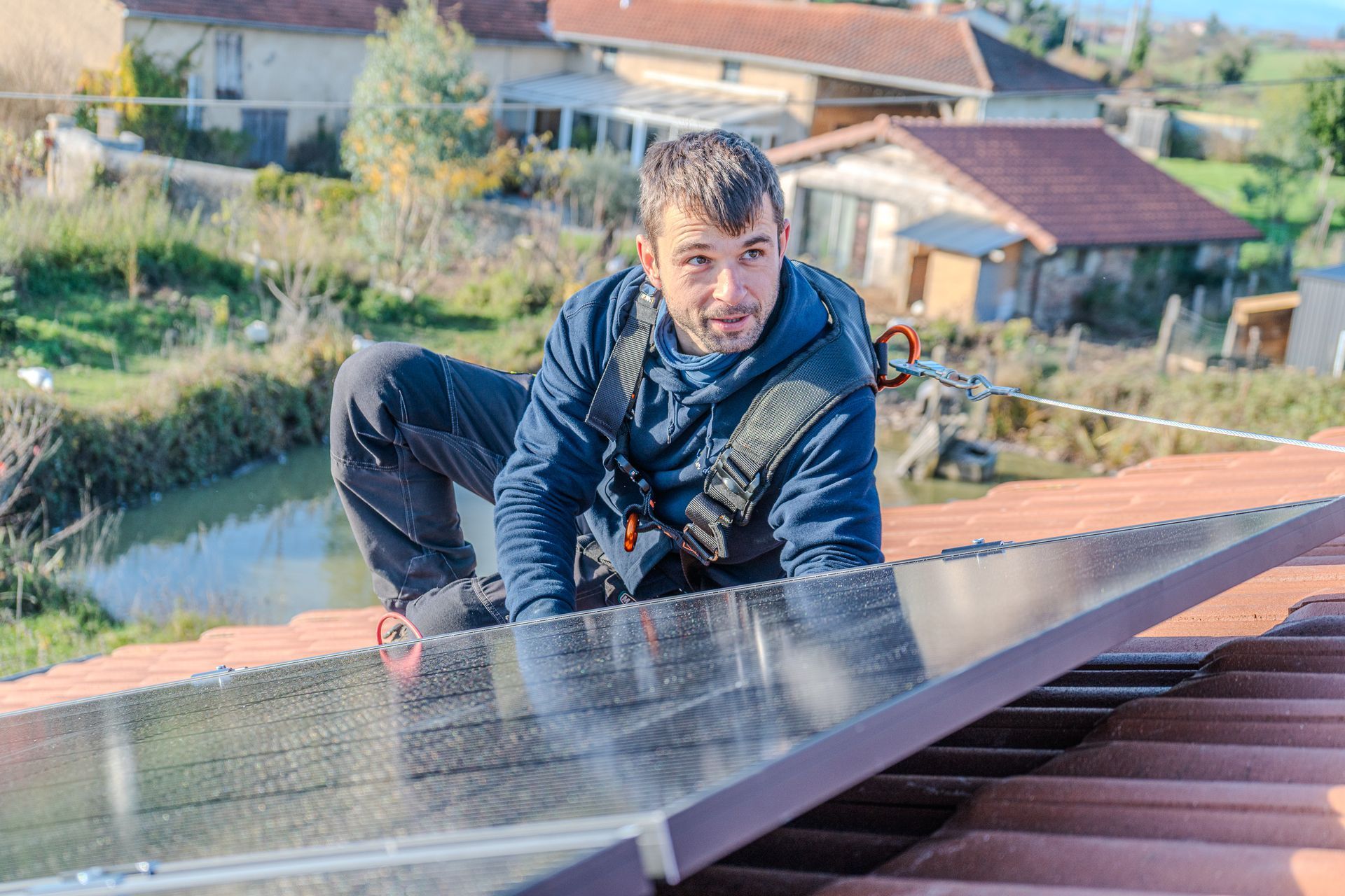 Un homme harnaché installe un panneau solaire sur un toit.