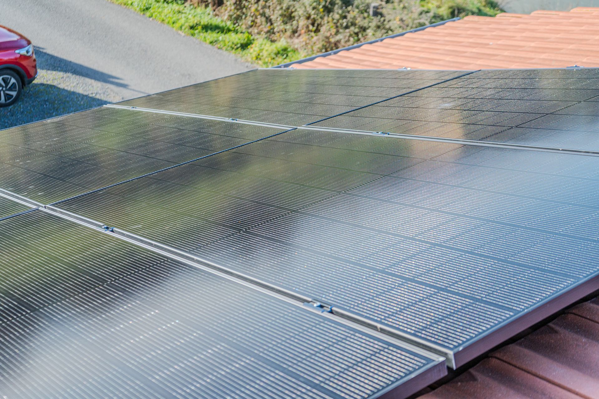 Panneaux solaires sur un toit en tuiles de terre cuite, une roue de voiture visible en haut à gauche.
