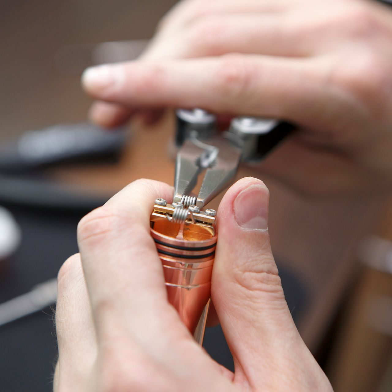Personne utilisant une pince pour ajuster une bobine de vapotage sur un appareil de vapotage de couleur cuivre.