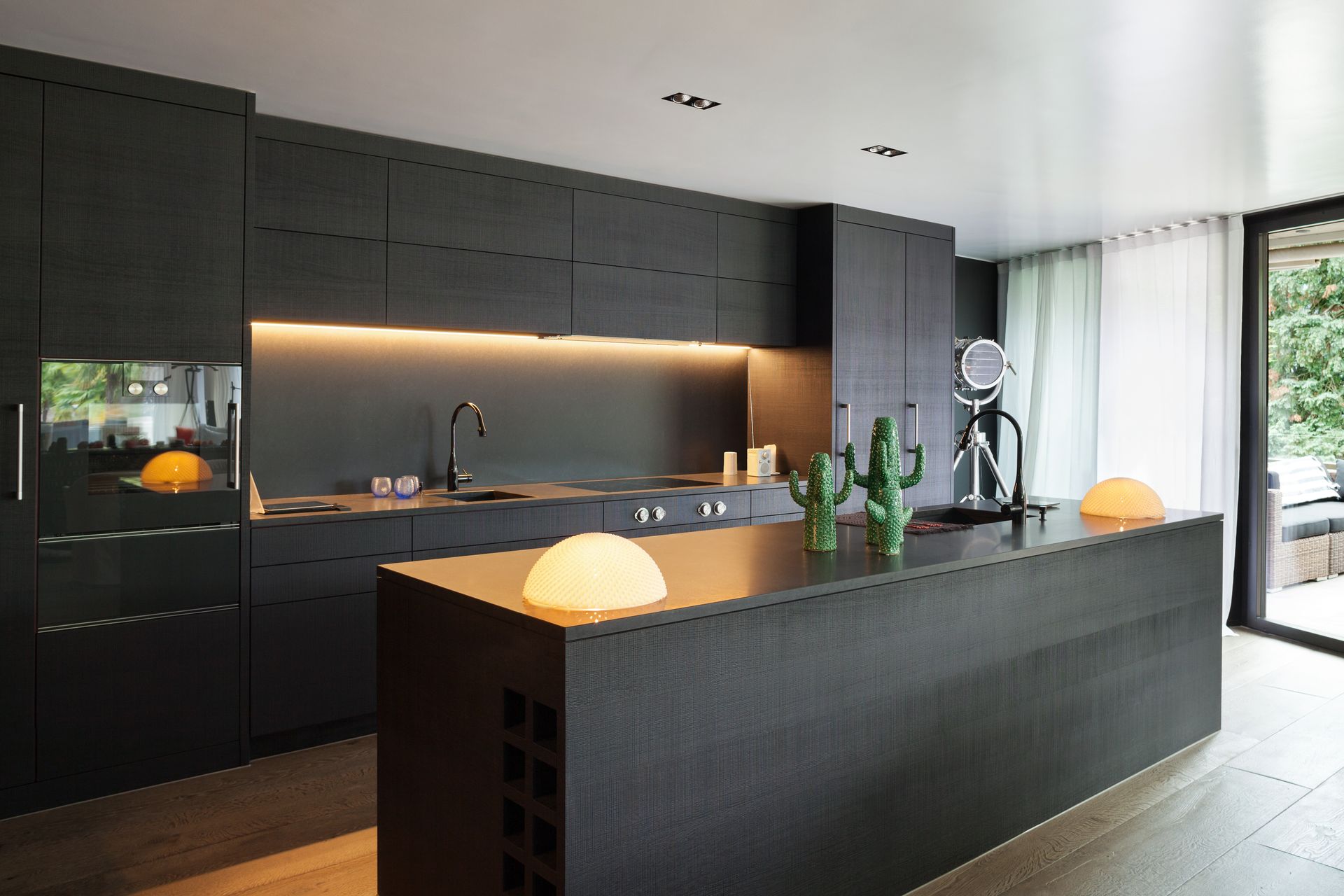 Cuisine moderne avec des armoires d'un noir mat, un grand îlot central, des lampes en forme de globes lumineuses et une décoration sur le thème des cactus.