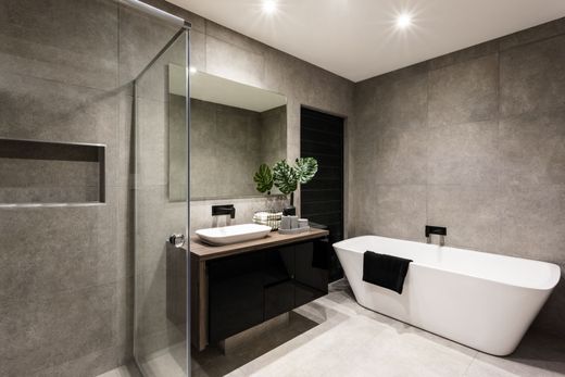 Une salle de bains moderne avec une baignoire à îlot blanche, un meuble lavabo foncé avec vasque et des murs carrelés imitation pierre grise.