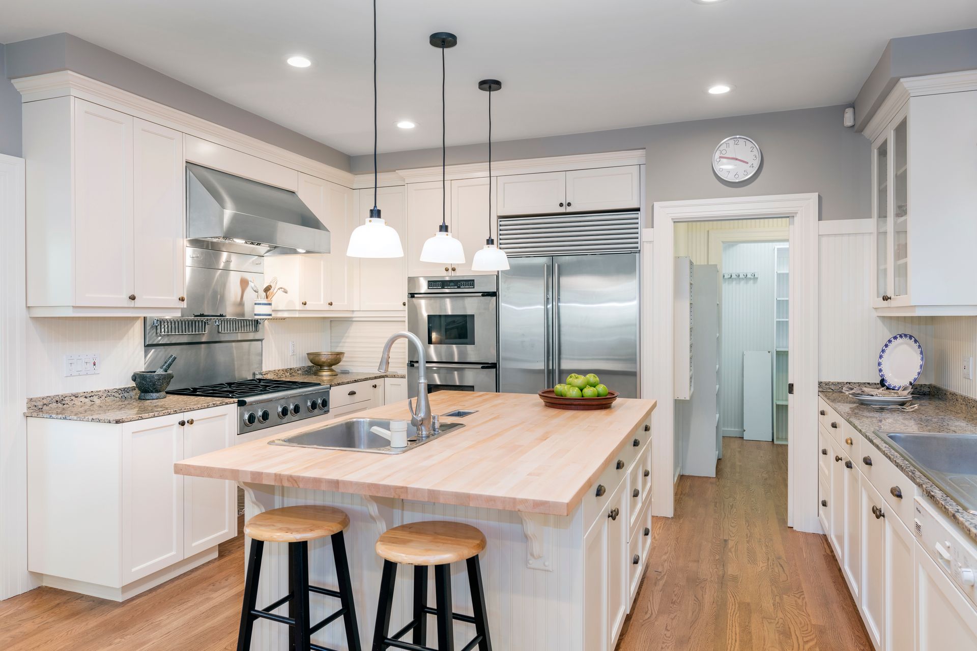 Une cuisine moderne et lumineuse avec des placards blancs, un îlot central en bois avec deux tabourets et des appareils électroménagers en acier inoxydable.
