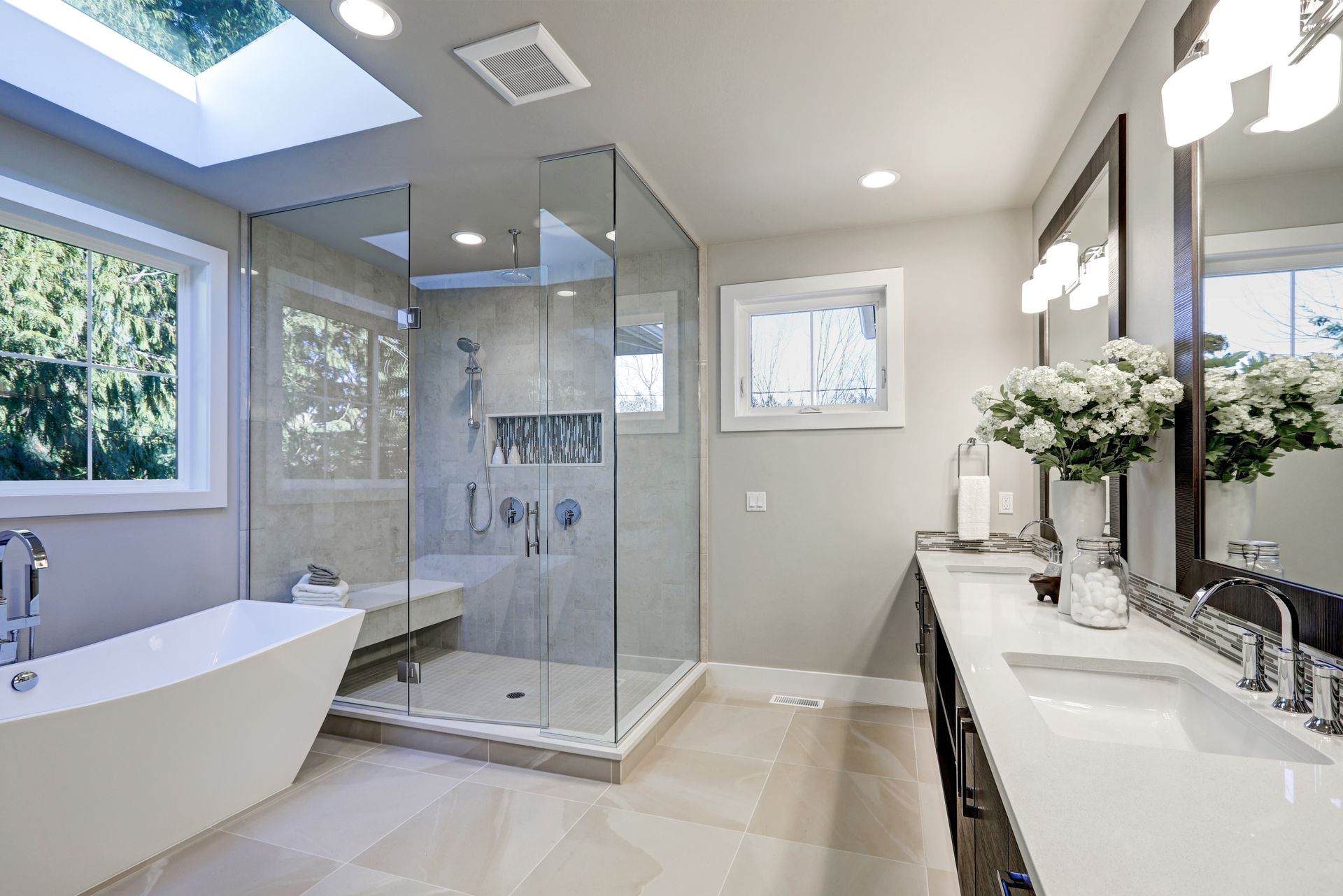 Salle de bains moderne avec douche vitrée, baignoire îlot, double vasque et puits de lumière.
