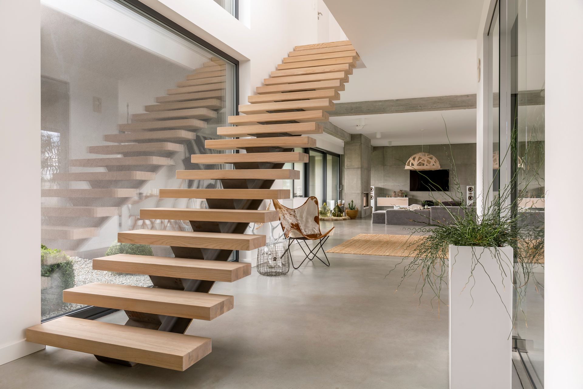 Un escalier flottant moderne avec des marches en bois clair et une structure métallique sombre, dans un espace de vie minimaliste et baigné de lumière.