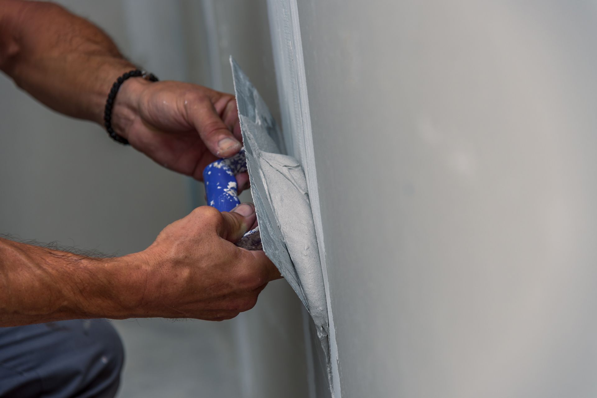 Une personne utilise un couteau à mastic métallique pour appliquer un enduit blanc sur un mur intérieur lisse.