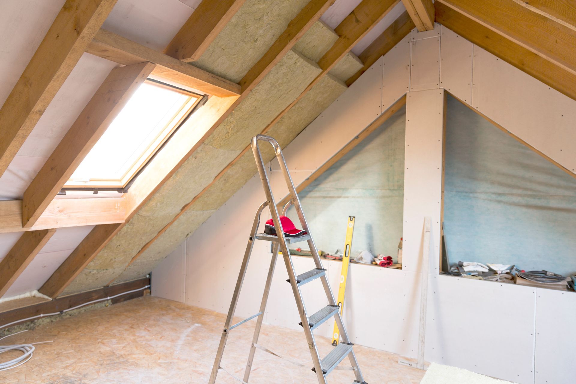 Rénovation des combles en cours, avec poutres en bois, puits de lumière, isolation, cloisons sèches et escabeau.