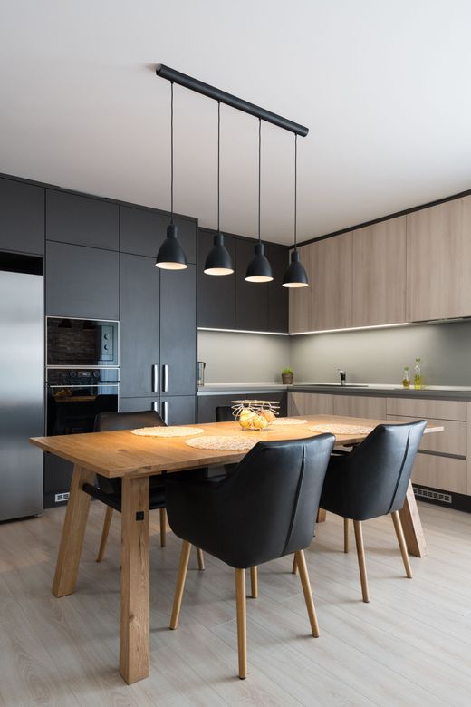 Un coin repas avec une table rustique en bois et quatre chaises noires modernes, sous un luminaire suspendu noir à quatre lumières.